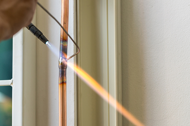 A technician brazing a copper refrigerant line with an oxy torch