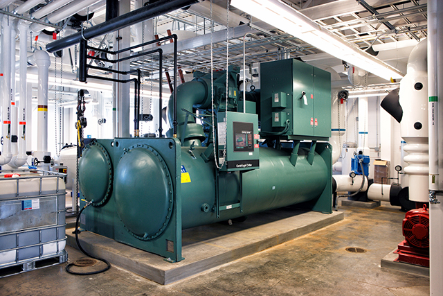 A green screw chiller with chilled-water pipework in a plant room